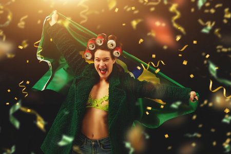 Young emotional woman, sports fan cheering up favorite Brazil football, soccer team over dark background with confetti. Winning gameの写真素材