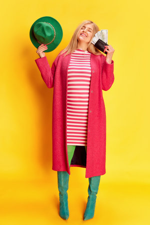 Portrait of woman in colorful clothes emotionally posing with money against yellow studio backgroundの写真素材