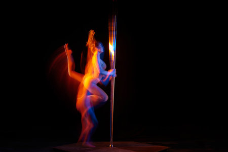 Strong muscular body. Young girl performing pole dance isolated over black studio background with mixed neon lights. Concept of art, sport and modern danceの写真素材