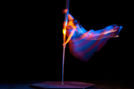 Strong hands. Young girl dancing, performing pole dance isolated over black studio background with...