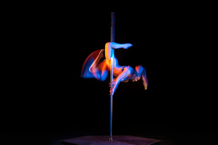 Gymnastic tricks. Young girl performing pole dance isolated over black studio background with mixed neon lights. Concept of art, sport and modern danceの写真素材