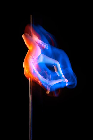 Artistic lifestyle. Young girl in bodysuit performing pole dance isolated over black studio background with mixed neon lights. Concept of art, sport and modern danceの写真素材