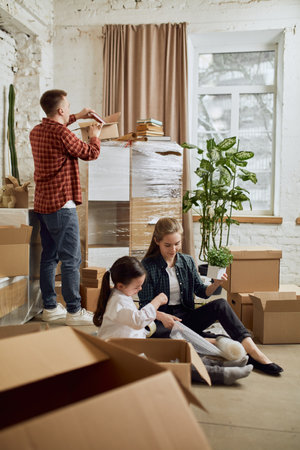 Young happy family, man, woman and kid moving into new flat, apartment. Opening many cardboard boxes and decorating roomの写真素材