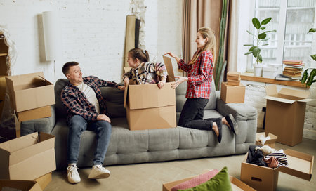 Playful parents and little daughter. Having fun. Young happy family, man, woman and kid moving into new apartment with many cardboard boxesの写真素材