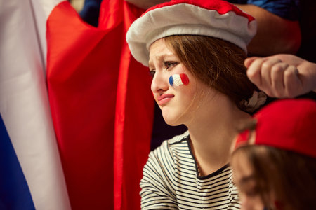 Young girl emotionally watching live football, soccer championship. Girl sitting with sad face because of losing game momentの写真素材