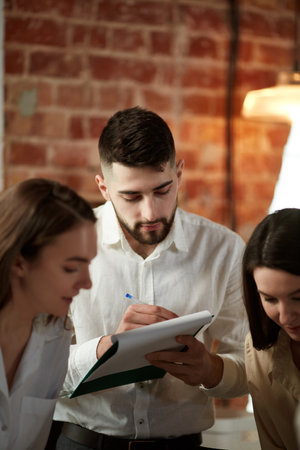 Young man, team leader in official clothes at business meeting with colleagues at office. Signing documents, checking strategiesの写真素材