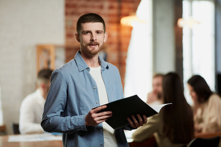 Teamleader of IT company. Young ambitious man in official clothes looking at camera in office. Blurred employees on backgroundの写真素材