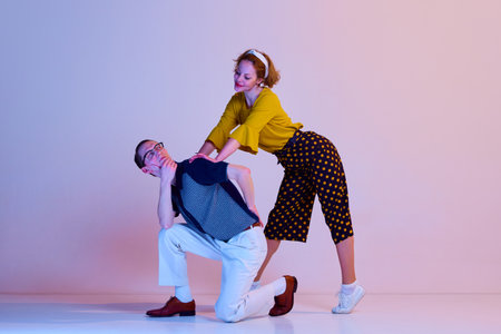 Emotional young couple, man and woman in stylish clothes dancing retro dance against gradient pink...