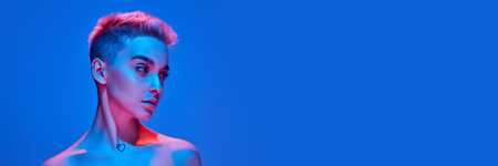 Young beautiful girl with blonde short hair posing against blue studio background with pink neon lightの写真素材