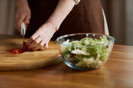 Close-up image of female hand cutting tomatoes on cutting board. Woman cooking healthy vitamin salad with fresh vegetables at homeの写真素材