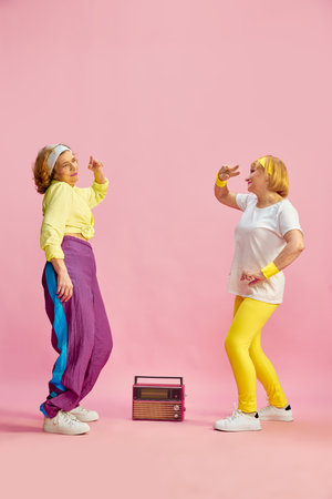 Two middle-aged, elderly, sportive woman in colorful uniform listening to radio and dancing, posing...