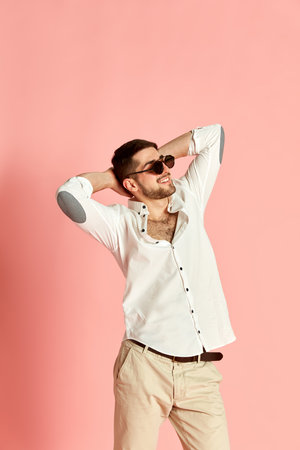 Portrait of handsome young man in stylish clothes and sunglasses posing with pleasant relaxed face against pink studio backgroundの写真素材
