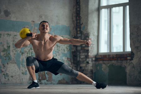 Legs exercises. Young sportive man with strong muscular, relief, shirtless body training with heavy weigh indoors on daytime. Concept of sportive lifestyleの写真素材