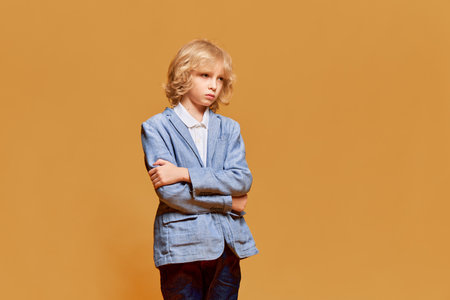 Little boy, child with blonde curly hair posing with calm, serious and bored face against orange studio background. Childhood and emotionsの写真素材