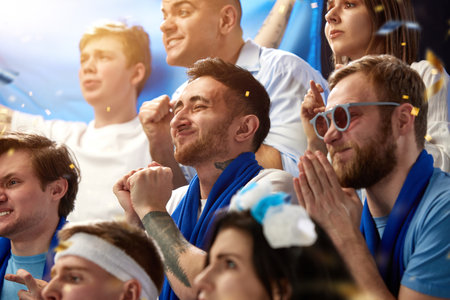 Support. Sport football fans watching greece soccer match, emotionally cheering team at stadium during gameの写真素材