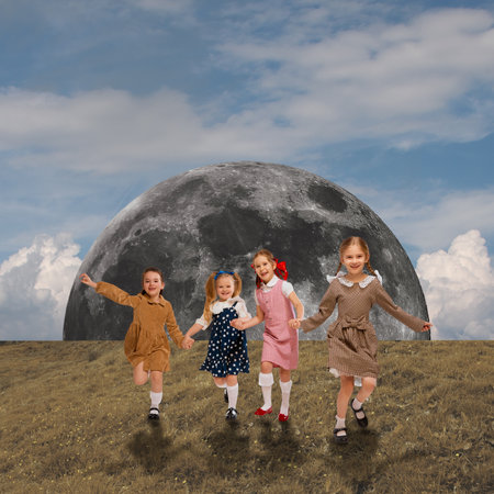 Playful, happy, little girls holding hands and running on green grass with giant moon on background. Childhood fantasy. Contemporary art collage.の写真素材