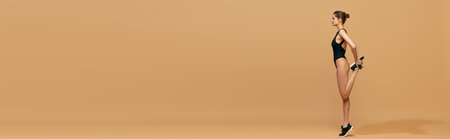 Warming-up before workout. Beautiful young girl with slim body in bodysuit training against orange studio backgroundの写真素材