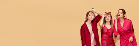 Funny faces. Pretty young girls in pajamas and robes taking care after skin with massage tools against studio backgroundの写真素材