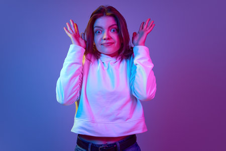 Emotional young girl with big eyes looking at camera with questioning face, posing against gradient...