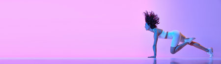 Dynamic image of young sportive woman in comfortable sportswear training against gradient pink blue background in neon lightの写真素材