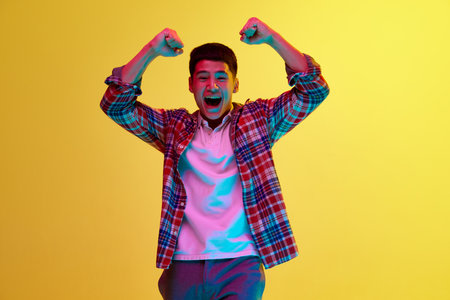 Young korean guy in stylish casual clothes showing emotions of success, win against yellow background in neon light. Achievement. Concept of human emotions and lifestyleの写真素材