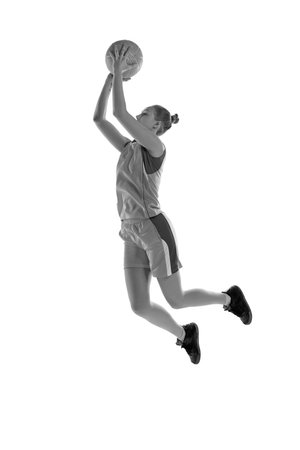 Black and white image of young athletic girl in jump, playing basketball against white studio background. Concept of professional sportの写真素材