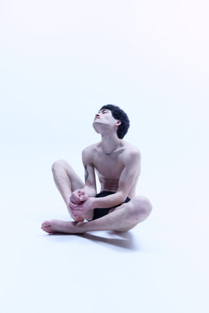 Studio portrait of young man posing shirtless, sitting on floor against white background.の写真素材