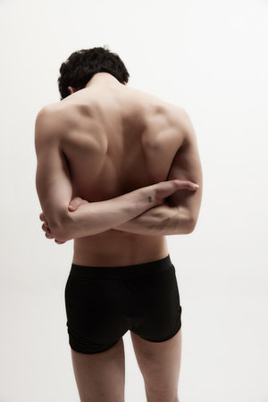 Relief, strong, muscular back. Rear view of young man posing shirtless, in black underwear against white studio background. Healthy spineの写真素材