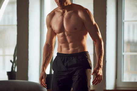 Cropped image of muscular, relief, strong, beautiful body. Male model posing shirtless, training at home on daytime.の写真素材