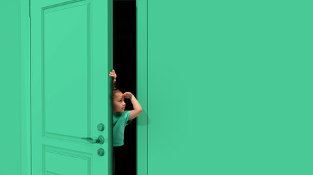 Little cute girl, kid peeking out green door with and to forehead. Playful mood, having fun. Curious kid looking with attentionの写真素材
