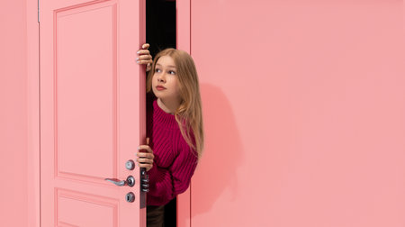Beautiful, young, blonde teen girl peeking out pink door and looking with attention, Overhearing secrets. Curiosityの写真素材