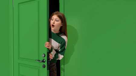 Astonished young girl, teengager peeking out green door with shocked face, looking with wide open eyes. Surpriseの写真素材