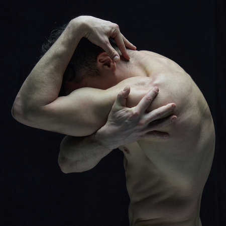 Artistic representation. Muscular man with relief body osig shirtless, with round back and hidden face against black studio backgroundの写真素材