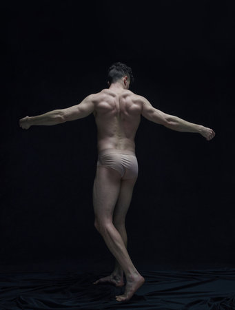 Full-length portrait of handsome shirtless man with muscular, relief body posing against black studio backgroundの写真素材