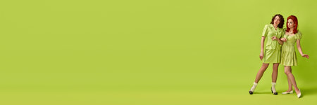 Portrait of two pretty young woman with stylish hairdo emotionally posing against green studio background. Retro fashion, pin-up, 60sの写真素材