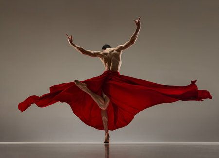 Talented performance. Handsome man, ballet dancer dancing with red silk fabric against grey studio backgroundの写真素材