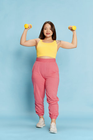 Full-length portrait of young, pretty, asian girl in pink and yellow sportswear standing with...