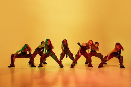 Contemp dance, hip-hop. Group of little girls, children, in stylish sportive clothes dancing against yellow studio background in neon lightの写真素材