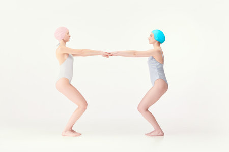 Two young girls, swimming athletes in retro style swimsuits standing in jump position isolated over white backgroundの写真素材