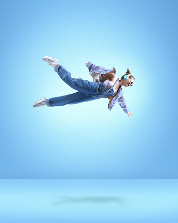 Stylish young girl in casual clothes, in headphones, flying over blue background. Creative ideas and...