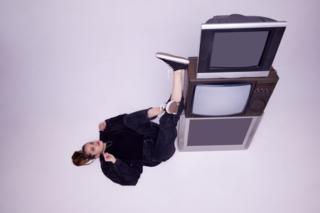 Top view. Beautiful young girl in jeans clothes lying on floor near retro tv sets over grey studio background. News, informationの写真素材