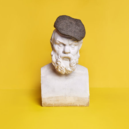 Antique statue bust with serious male expression wearing cap against yellow backgroundの写真素材