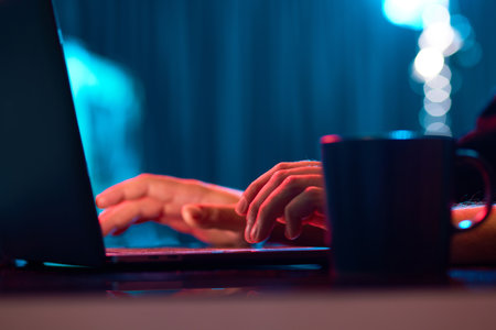 Businessman working remotely, typing on laptop keyboard over neon lights. Working with online projectsの写真素材