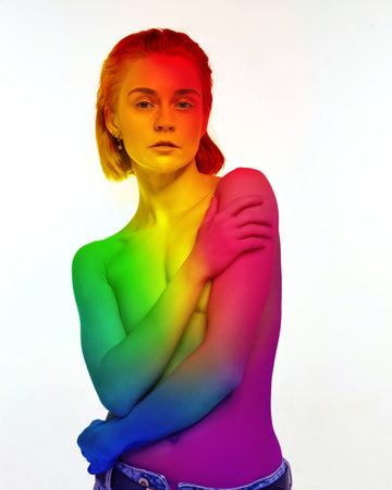 Portrait of young beautiful, tolerant woman standing shirtless with body colored in rainbow colors against white background. Lgbt supportの写真素材