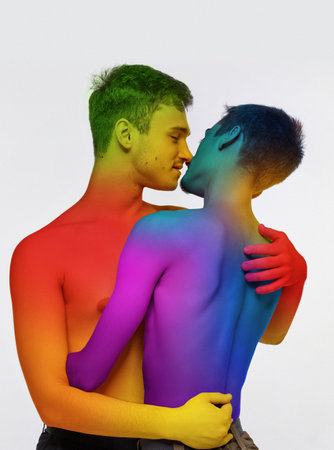 Portrait of two loving young men, couple hugging, kissing against white background. Models posing shirtless with rainbow colored bodyの写真素材