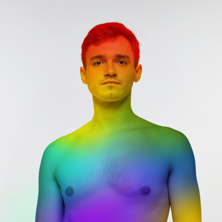 Portrait of young man posing shirtless with body colored in rainbow colors over white background. Lgbt supporter. Acceptance of beingの写真素材