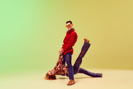 Retro party. Emotional expressive young man and woman in vintage style outfits dancing against gradient green yellow backgroundの写真素材