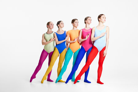 Group of young girls, professional ballet dancer in colorful bodysuits and tights standing in position against grey studio backgroundの写真素材