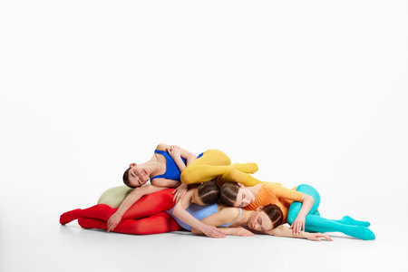 Group of tender, young girls, ballet dancers in colorful, bright clothes lying on each other on floor, dancing against grey studio backgroundの写真素材