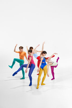 Group of talented, artistic female ballet dancers in bright, multicolored clothes performing, dancing against grey studio backgroundの写真素材